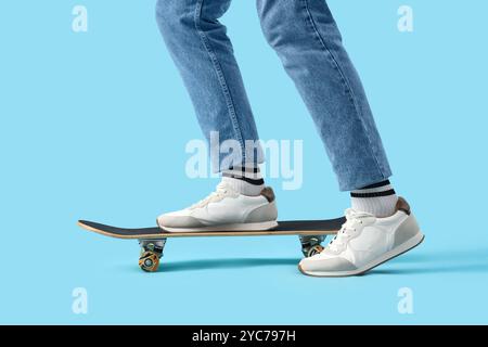 Junger Mann in Turnschuhen mit Skateboard auf blauem Hintergrund Stockfoto