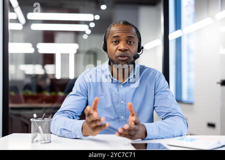 Reifer Geschäftsmann mit Headset in modernen Büros, der Videoanrufe führt und Geschäftsstrategien diskutiert. Ruhiges und fokussiertes Verhalten im professionellen W Stockfoto