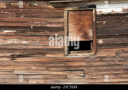 Alte hölzerne Außenwand eines Gebäudes mit Fenster die alte hölzerne Außenwand des Gebäudes, die oben verschlossen ist, zeigt verwitterte Abstellgleise ohne Farbspuren. Stockfoto