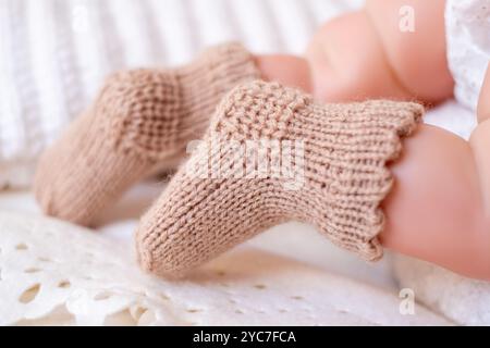 Kuschelige, handgestrickte Stiefeletten schmücken sanft die Füße eines friedlichen Säuglings, das auf einer gemusterten Decke in einem warmen, einladenden Kinderzimmer liegt. Stockfoto