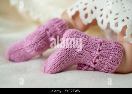 Diese kuscheligen, pinkfarbenen Babyschühchen sind mit komplizierten Strickmustern versehen und sorgen für Wärme für kleine Füße, die sanft auf einer weichen weißen Decke liegen. Stockfoto