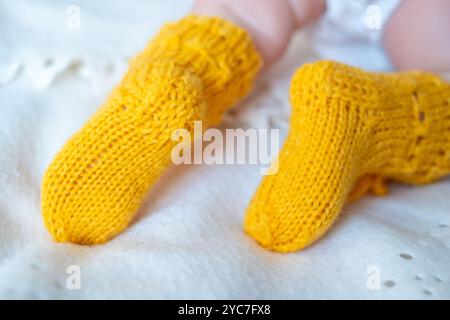 Ein Baby mit kleinen Füßen trägt leuchtend gelbe Stricksocken, die bequem auf einer flauschigen weißen Decke liegen und in das sanfte Morgenlicht eintauchen. Stockfoto