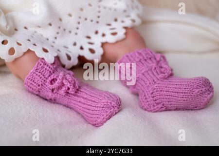 Ein Paar niedlicher rosafarbener Strickschühchen schmückt die Füße eines Säuglings, das auf einer weichen Decke liegt. Die gemütliche Umgebung bietet einen warmen Nachmittag in Hom Stockfoto