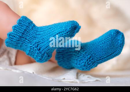 Zwei bezaubernde blaue Babyschuhe liegen auf einer weichen weißen Decke und betonen ihre gestrickte Textur und leuchtende Farbe, ideal um wenig Geld zu behalten Stockfoto