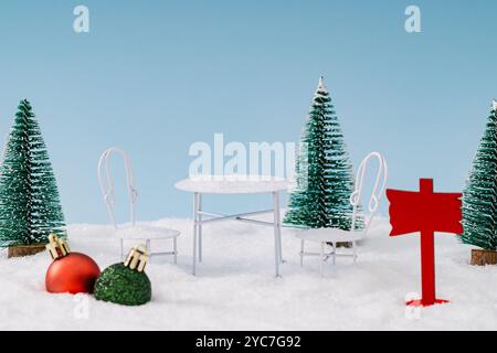 Winterkomposition mit grünen Weihnachtsbäumen Weihnachtskugeln, weißem Tisch und Stühlen und Schnee auf blauem Hintergrund. Minimales Weihnachts- und Neujahrskonzept Stockfoto