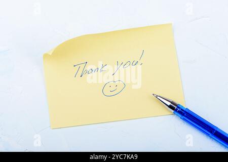 Ein gelbes Schreibpapier mit fröhlichem Bild und handschriftlicher Inschrift: Danke. Kopierbereich. Stockfoto