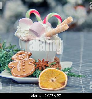 Die Tasse enthält Kakao, verziert mit Schlagsahne und Marshmallows. Zuckerstangen und Waffelbrötchen sind wunderschön angeordnet. Das Getränk wird mit serviert Stockfoto