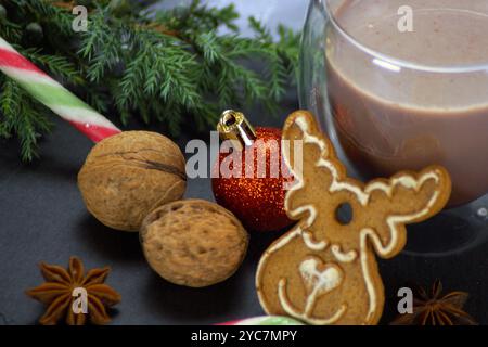 Zwei Klarglasbecher gefüllt mit heißem Kakao, ein Lebkuchenkeks in Form eines Weihnachtsbaums, ein Tannenzweig, Nüsse und ein Zuckerrohr ergänzen das Stockfoto