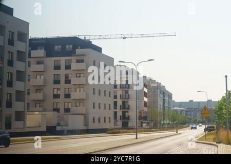 Ein Baukran ragt über neuen Wohngebäuden auf einer sonnendurchfluteten Straße. Die lebhafte Szene fängt die städtische Entwicklung in einem warmen, einladenden atmos ein Stockfoto