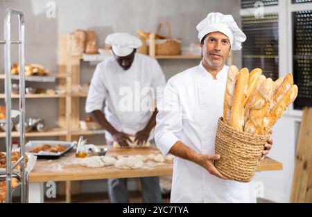 Professioneller Bäcker, der frische französische Baguettes in der Bäckerei präsentiert Stockfoto