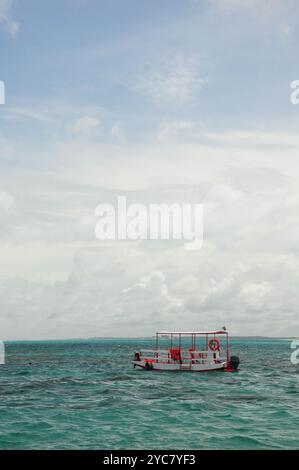 Einsames Boot, das in ruhigem türkisfarbenem Wasser unter einem weiten, bewölkten Himmel driftet. Stockfoto