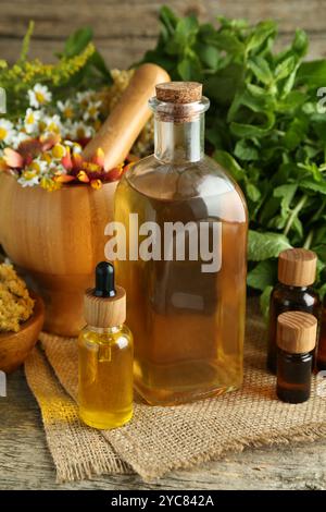 Tinkturen in Flaschen, Heilkräuter und Mörtel mit Stößel auf Holztisch Stockfoto