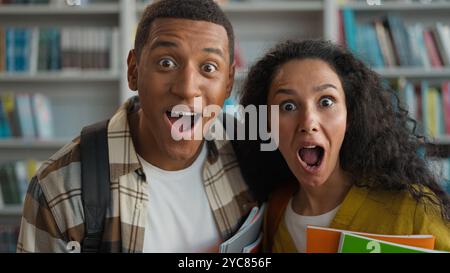 Schockierter afroamerikanischer Mann Hispanic Kaukasierin Studenten Klassenkameraden High School Universitätsbibliothek offener Mund erstaunliche Überraschung Wunderfragen Stockfoto