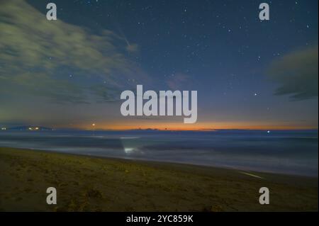 Der Sonnenuntergang an der Küste verwandelt sich in eine sternenklare Nacht. Im Himmelskomet C/2023 A3 (Tsuchinshan ATLAS), Sterne und Wolken, San Vincenzo, Italien Stockfoto