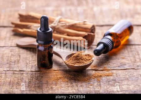 Eine hölzerne Oberfläche mit einer kleinen Flasche ätherischen Zimtöls, einem Löffel Zimtpulver und Zimtstangen, die mit Garn gebunden sind. Stockfoto