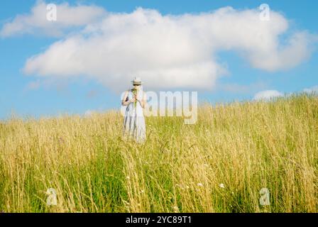 Glückliche reife Frau mit Wildblumen auf einem hohen Grasfeld an einem hellen Sommertag. Stockfoto