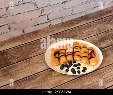 Pfannkuchen gefüllt mit Hüttenkäse, garniert mit Karamell, Sauerrahm und Heidelbeeren auf einem Holztisch. Nahaufnahme. Stockfoto