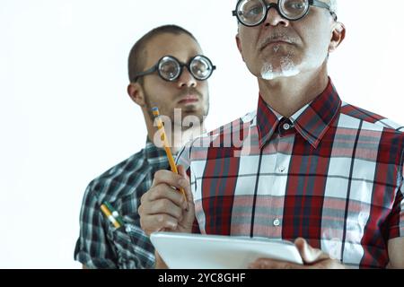 Zwei nervöse Wissenschaftler mit dicker Brille machen sich Notizen, während sie Daten auf einem Tablet überprüfen und möglicherweise an einem Forschungsprojekt zusammenarbeiten Stockfoto