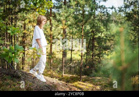 Ein kleines Kind spaziert ruhig auf einem Waldweg und genießt die Wärme der Sonne und die Ruhe der umliegenden Bäume und Pflanzen Stockfoto