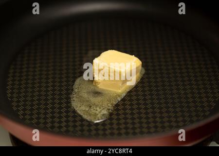 Ein Stück Butter wird in einer antihaftbeschichteten Pfanne geschmolzen, Nahaufnahme Stockfoto