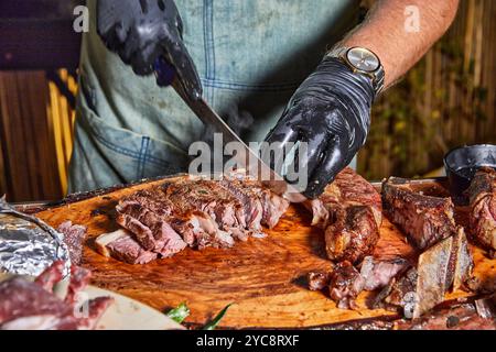 Ein Küchenchef in schwarzen Handschuhen schneidet ein dickes, saftiges Rindfleisch auf einem Holzbrett und offenbart sein perfekt gekochtes Interieur. Stockfoto