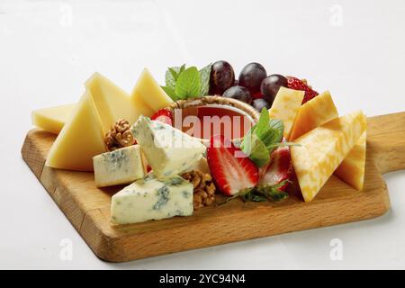 Verschiedene Käse- und Obstsorten auf dem Holzschreibtisch, darunter Blauschimmelkäse und gepressten Rohkäse sowie Honig und Walnüsse Stockfoto