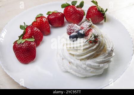 Nachtisch Pavlova und Erdbeeren auf weißem Teller und weißem Holztisch Stockfoto