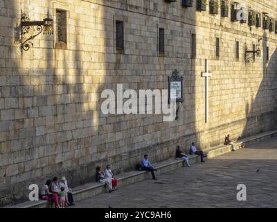 Die Menschen genießen das milde Herbstwetter auf der Steinbank entlang der steilen Mauer des Klosters San Paio de Antealtares auf dem Quintana-Platz (Praza) Stockfoto