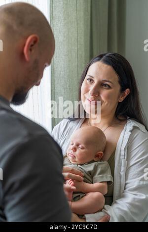 Familie mit neugeborenem Jungen. Eltern berühren sanft Baby und einander. Das Baby liegt leise in den Armen. Wärme und Harmonie in der Familie. Pflege und Stockfoto