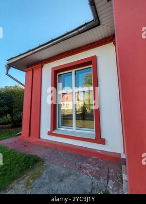 Ein Gebäude mit einem rot umrandeten Fenster in einer weißen Wand, das die Umgebung im Freien reflektiert. Dieses Foto unterstreicht den ästhetischen Reiz von Stockfoto