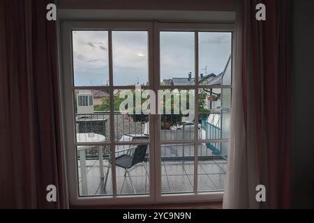 Blick durch geschlossenes Fenster in Regentropfen mit Vorhängen auf dem Balkon Stockfoto