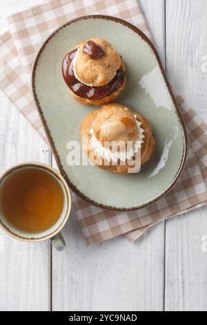 Französische Religieuse-Gebäck-Profiteroles mit Vanillecreme und Schokolade und Kaffeeglasur in einer Schüssel auf einem Holztisch. Vertikale Draufsicht von einem Stockfoto