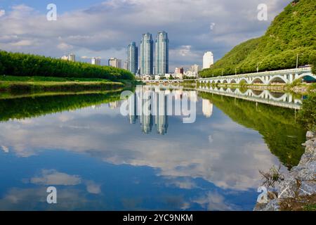 Ulsan, Südkorea - 9. Juli 2019: Das ruhige Wasser des Taehwa River spiegelt die Skyline der Stadt und das üppige Grün entlang der Ufer wider und schafft so ein pict Stockfoto