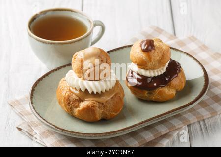 Exquisites Religieuse Eclair-Gebäck mit Patissiere-Creme mit Schokolade und Kaffeeglasur in einer Schüssel auf einem Holztisch. Horizontal Stockfoto