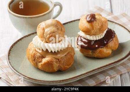 Religieuse Choux Brötchen gefüllt mit flauschiger Vanillecreme und Schokolade oder Kaffeeglasur in einer Schüssel auf einem Holztisch. Horizontal Stockfoto