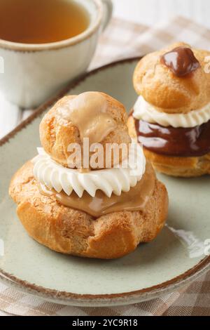 Französische Religieuse-Gebäck-Profiteroles mit Vanillecreme und Schokolade und Kaffeeglasur in einer Schüssel auf einem Holztisch. Vertikal Stockfoto