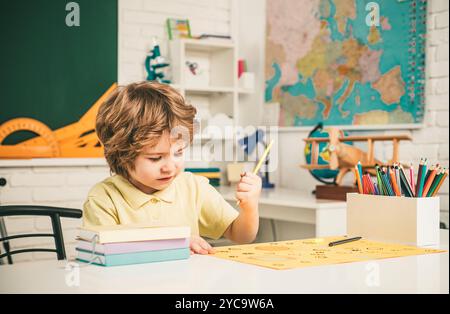 Nette Schüler mit lustigen Gesicht Schularbeit. Kinder machen sich bereit für die Schule. Freundliches Kind im Klassenzimmer in der Nähe der Tafel. Stockfoto