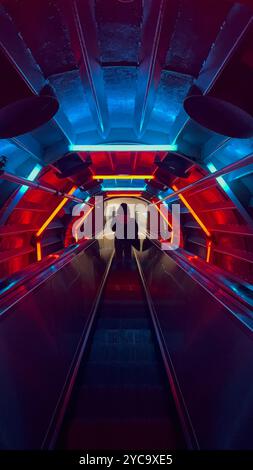 Frau, die eine Rolltreppe hinunterfährt, umgeben von bunten Neonlichtern im Atomium in Brüssel, Belgien. Stockfoto