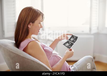 Frau, zu Hause und Lächeln für die Schwangerschaft mit Scan von Baby für Zukunft, Wachstum und Kind. Weibliche Person, Mutterschaft und glücklich oder zufrieden auf der Couch in Stockfoto