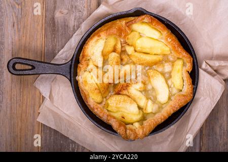Hausgemachte Apfeltorte in einer gusseisernen Pfanne, mit Scheiben goldener Früchte und knusprigem Blätterteig. Die heiße Pfanne ruht auf Backpapier über einem Rusti Stockfoto