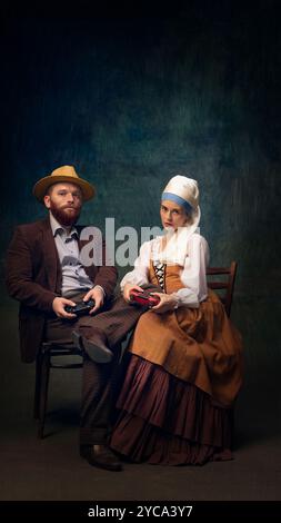 Kreatives Porträt eines eleganten Paares in Vintage-inspirierter Kleidung, das am Tisch sitzt und mit Gaming-Controllern spielt. Stockfoto