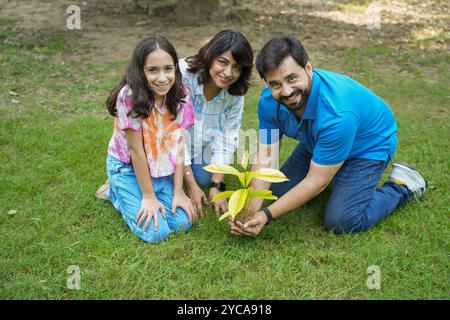 Glückliche junge indische Familie, die Baum pflanzt, während sie in die Kamera blickt. Konzept des Umweltschutzes, der Freiwilligen und der nachhaltigen Lebensweise. Stockfoto