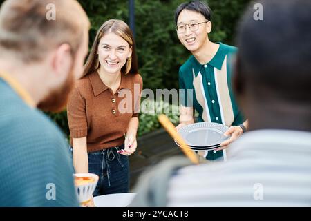 Gruppe fröhlicher erwachsener Freunde, die gemeinsam im Freien einen Tisch für die Abendparty bereiteten Stockfoto