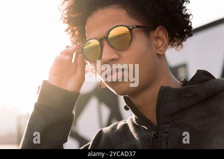 Männlicher Teenager mit lockigen Haaren, der Sonnenbrille anpasst Stockfoto