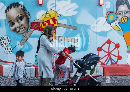 England, London, Southwark, muslimische Dame mit Kindern, die an farbenfrohen Reklametafeln vorbeilaufen Stockfoto