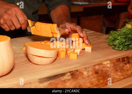 Ein afrikanischer schwarzer Koch schneidet Butternusskürbis auf einem hölzernen Schneidebrett in einer Küche Stockfoto