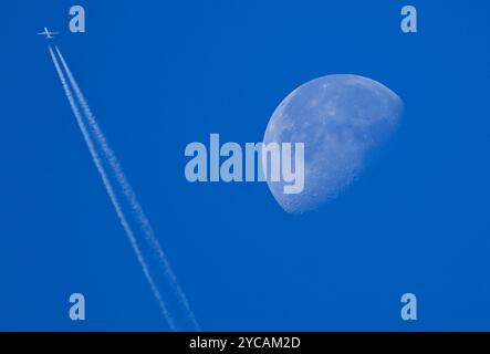 22. Oktober 2024, Hessen, Frankfurt/Main: Neben dem abnehmenden Mond lässt ein Passagierflugzeug Kondensstreifen am blauen Himmel über Frankfurt fliegen. Foto: Arne Dedert/dpa Stockfoto