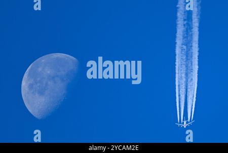 22. Oktober 2024, Hessen, Frankfurt/Main: Neben dem abnehmenden Mond lässt ein Passagierflugzeug Kondensstreifen am blauen Himmel über Frankfurt fliegen. Foto: Arne Dedert/dpa Stockfoto