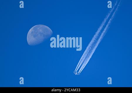 22. Oktober 2024, Hessen, Frankfurt/Main: Neben dem abnehmenden Mond lässt ein Passagierflugzeug Kondensstreifen am blauen Himmel über Frankfurt fliegen. Foto: Arne Dedert/dpa Stockfoto