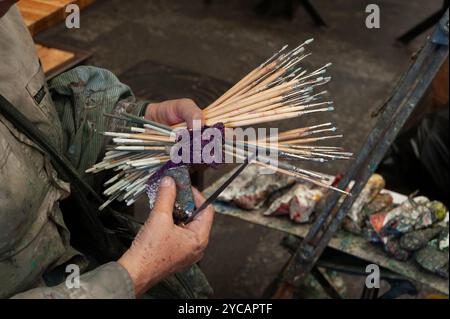 Eine Malerin fasst eine große Sammlung verschiedener Pinsel und Größen in ihrer Hand, die während einer Ölmalerei verwendet wurden. Stockfoto